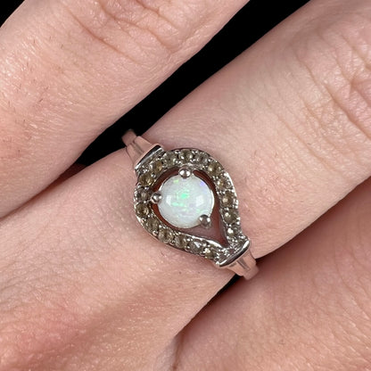 Close-up of round Australian white opal and smoky quartz women's ring, worn on finger; the opal has green flashes of color