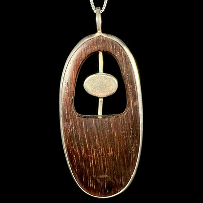 Back side of a rustic, hand-carved wood men's pendant with a sterling silver bezel surrounding the dark brown wood.