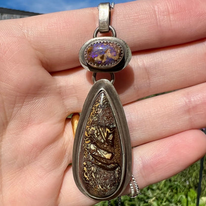 Rustic silver boulder opal pendant held in a hand against a natural background in daylight.