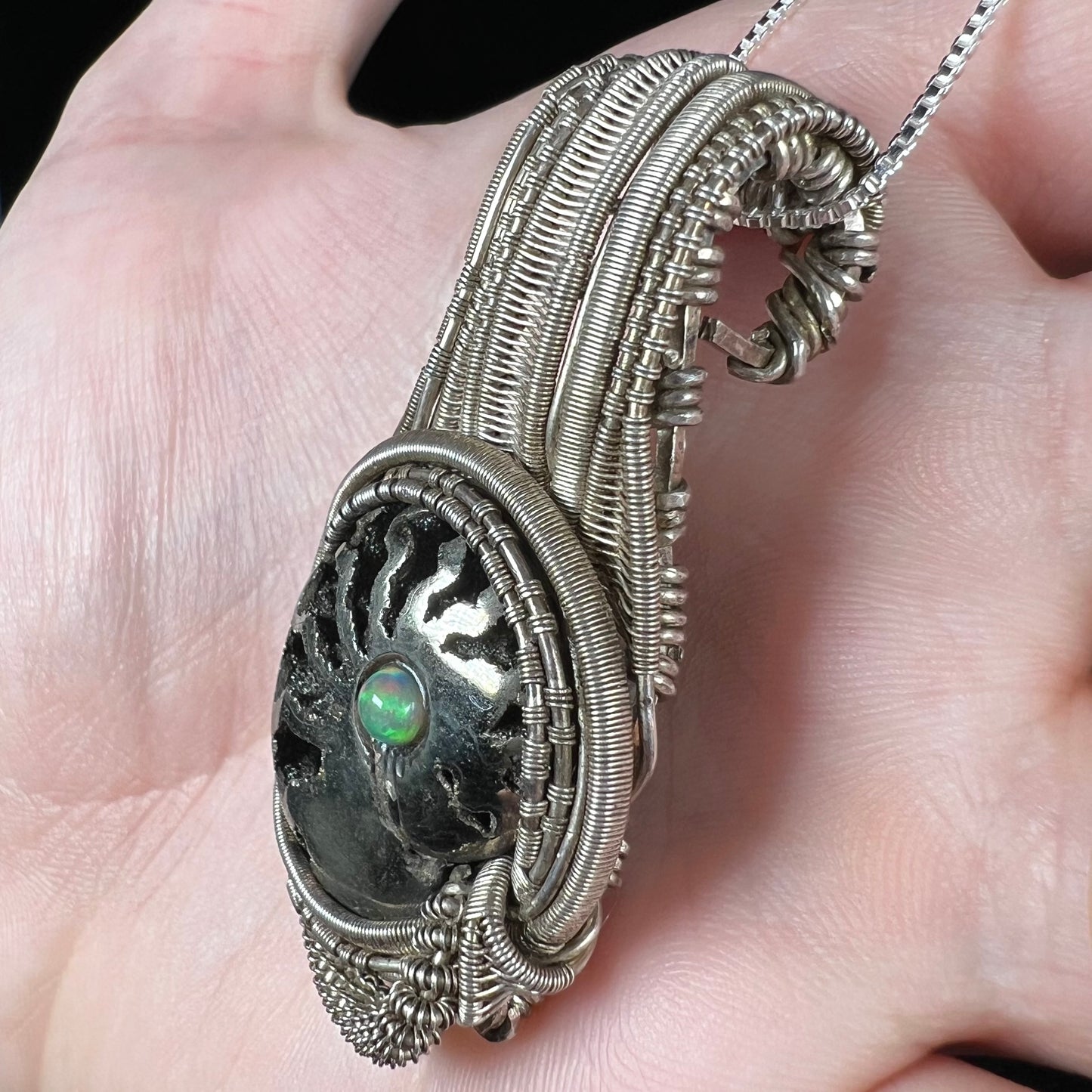 Rustic style wire-wrapped men's pendant set with a pyritized ammonite and Ethiopian opal accent, shown from side view in hand.