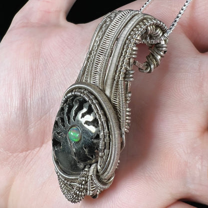 Rustic style wire-wrapped men's pendant set with a pyritized ammonite and Ethiopian opal accent, shown from side view in hand.