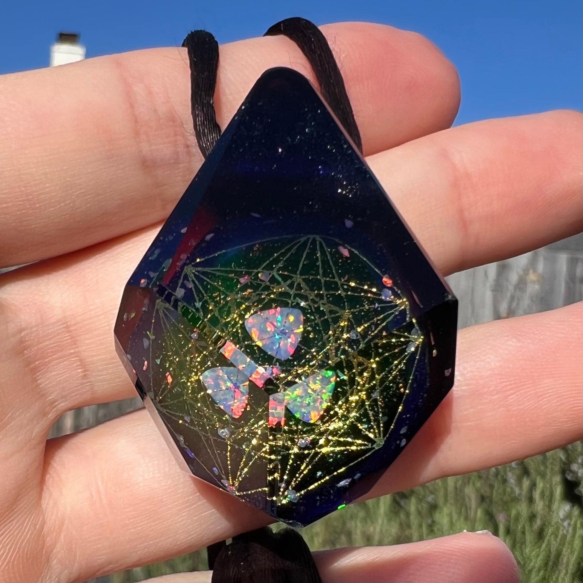 Sacred geometry is seen in a lab-created opal and glass pendant, featuring a hexagram design, held by a hand in the sunlight.