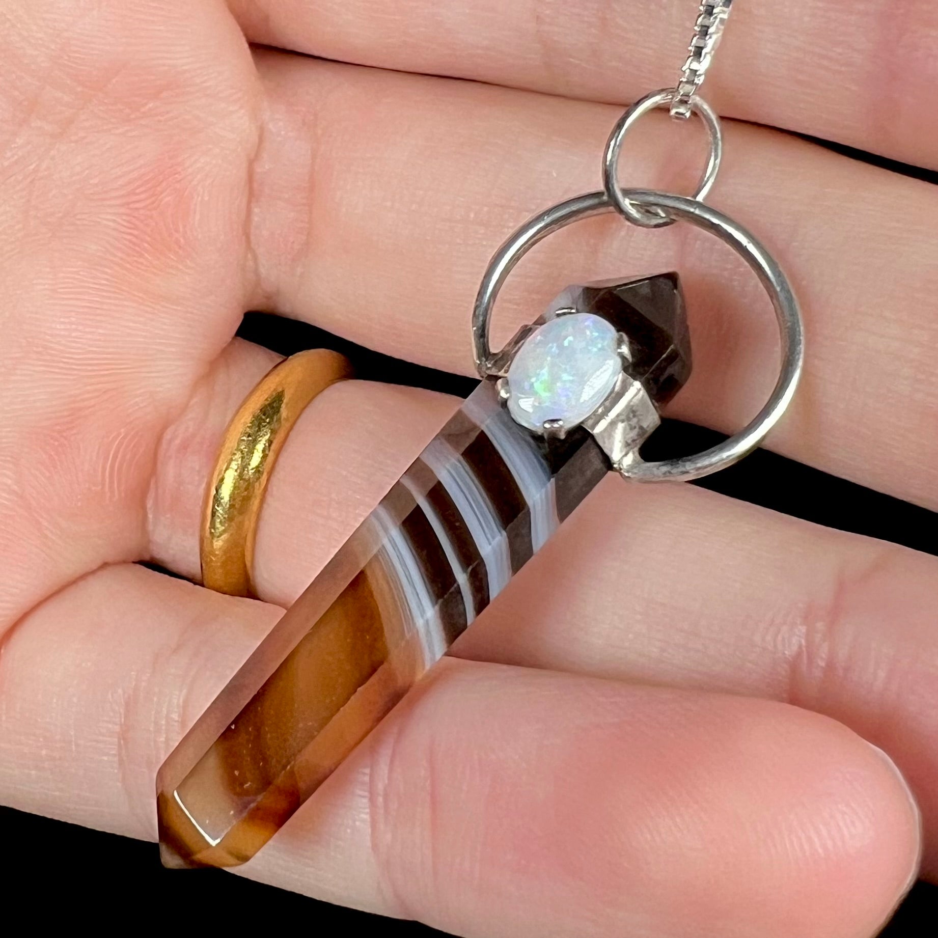A sardonyx crystal necklace with a white opal accent, held against black background in a hand.
