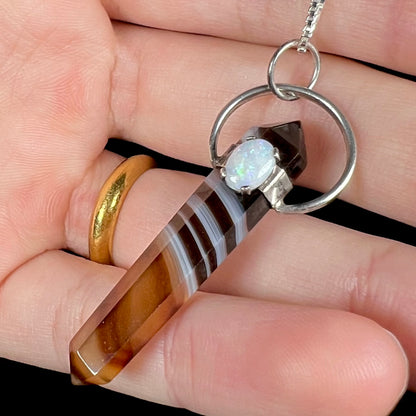 A sardonyx crystal necklace with a white opal accent, held against black background in a hand.