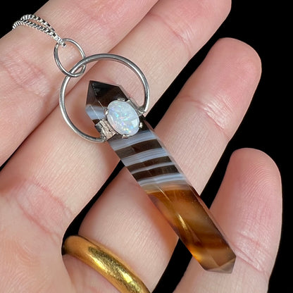 A sardonyx and opal pendant in sterling silver, held in a hand against black background.