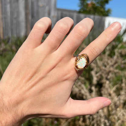 Hand wearing sculptural Modernist-style opal an diamond cocktail ring in sunlight; the ring has swooping gold design