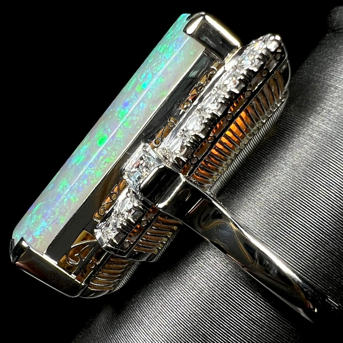 Side view of a large Australian semi-crystal opal mounted in a high-profile mid-century platinum mounting, a golden glow seen below opal through open filigree and ribbed basket design.