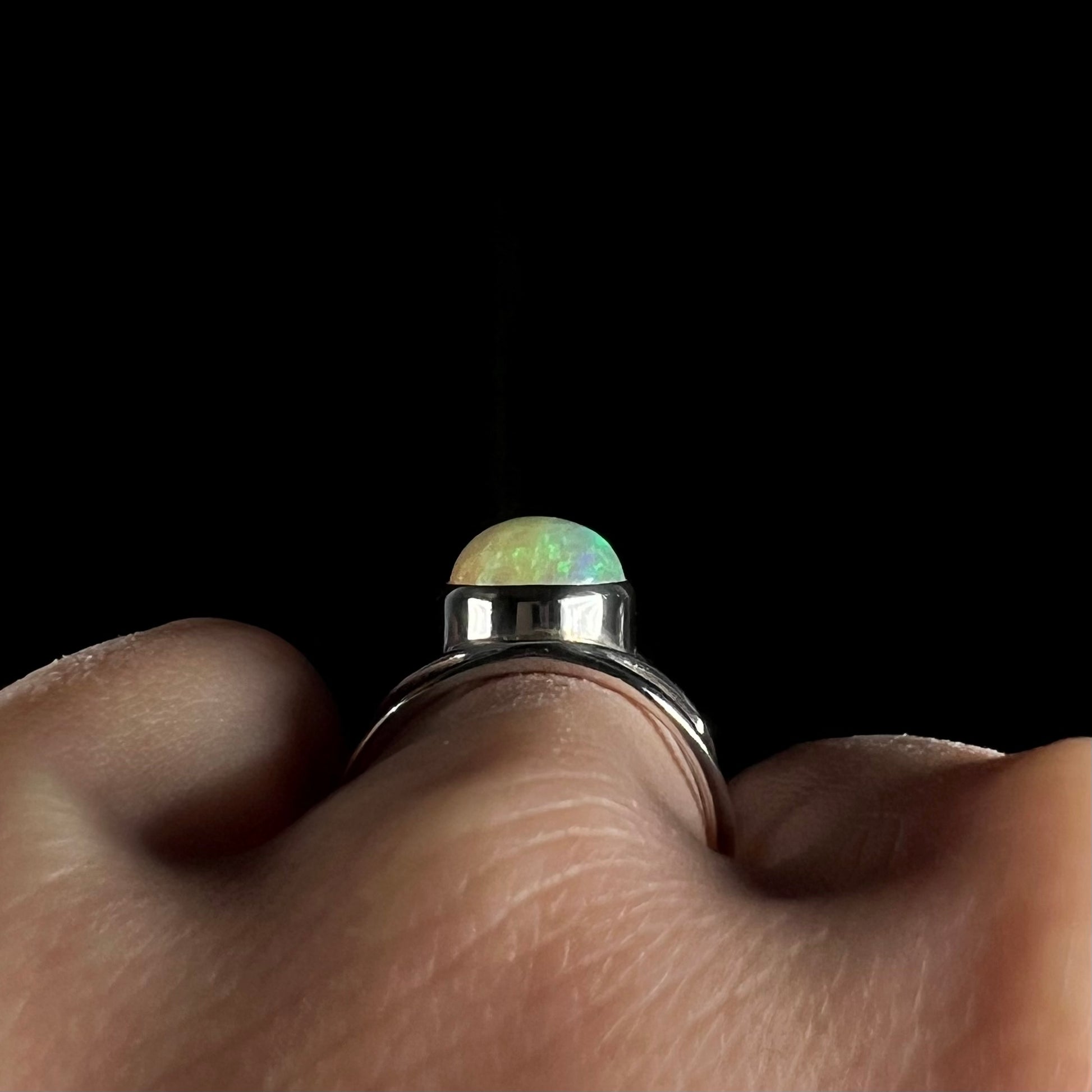 Side gallery view of a silver opal ring worn on a finger, shown against a dark background.