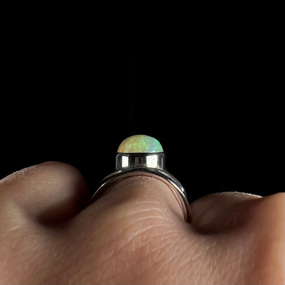 Side gallery view of a silver opal ring worn on a finger, shown against a dark background.