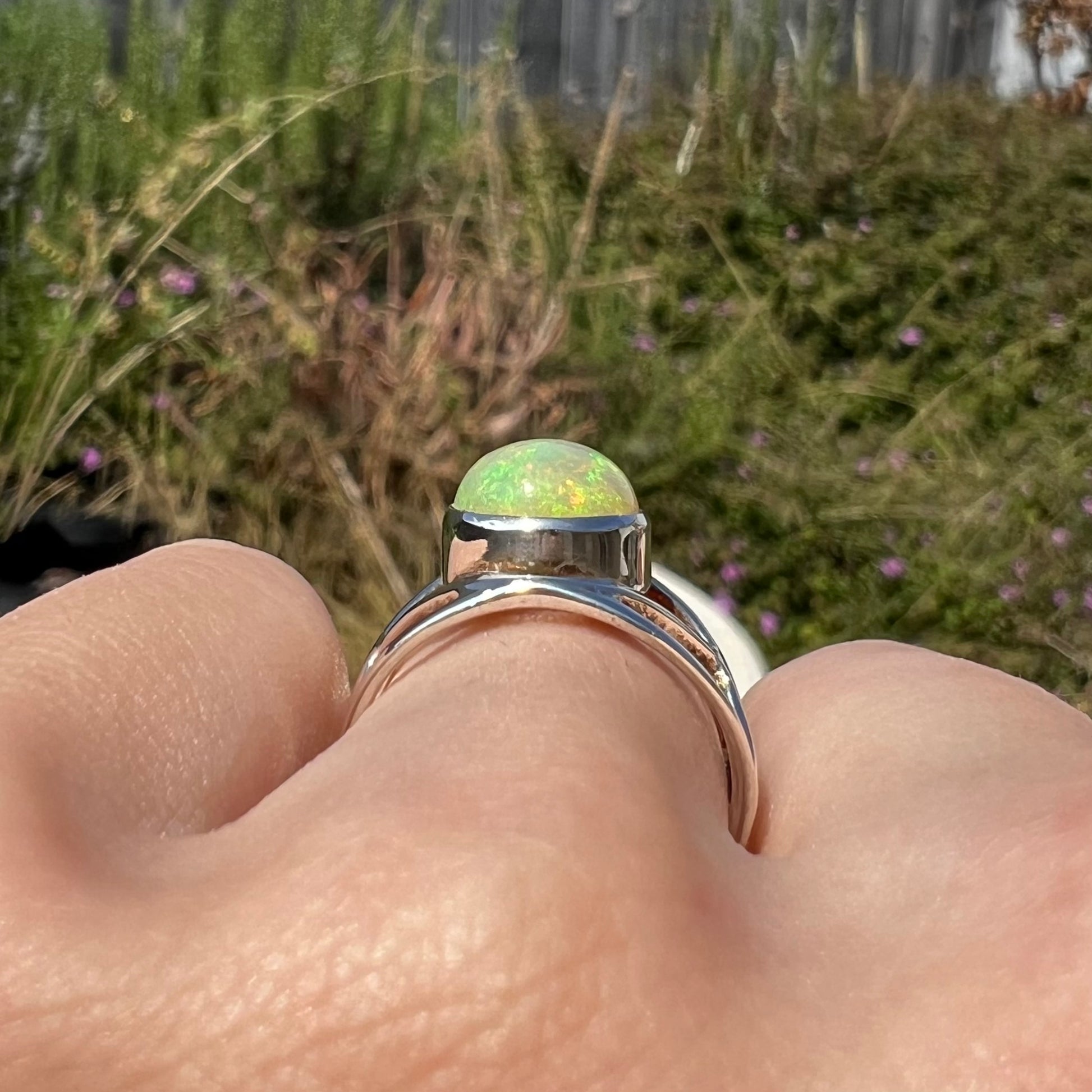 Side profile gallery view of a siver opal ring worn on a hand in an outdoor setting, showing the ring's bezel.
