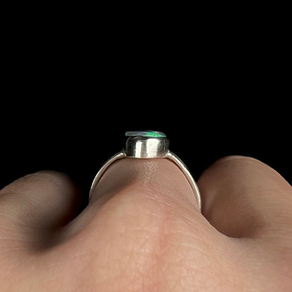 Side gallery profile view of a sterling silver opal solitaire ring, worn on a hand.