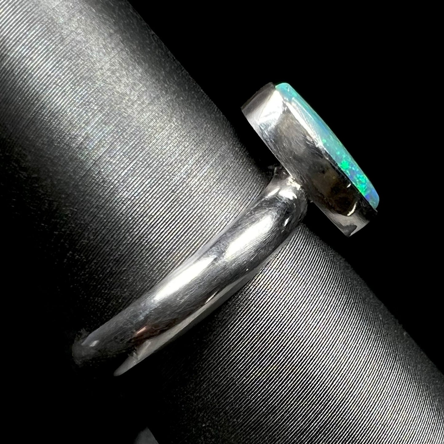 The shank and bezel setting side view of a simple sterling silver solitaire opal ring on a ring display.