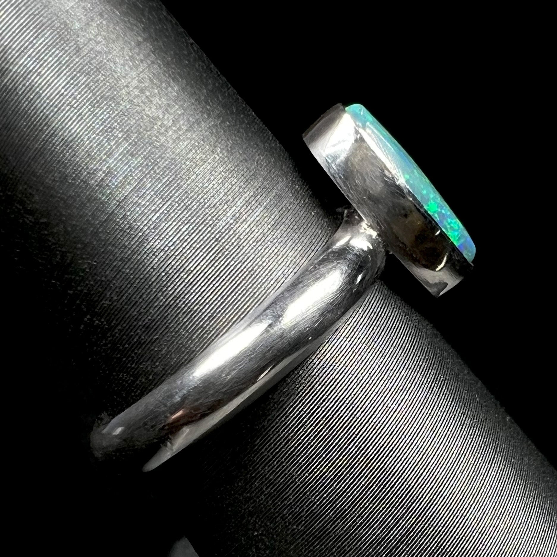 The shank and bezel setting side view of a simple sterling silver solitaire opal ring on a ring display.