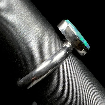 The shank and bezel setting side view of a simple sterling silver solitaire opal ring on a ring display.