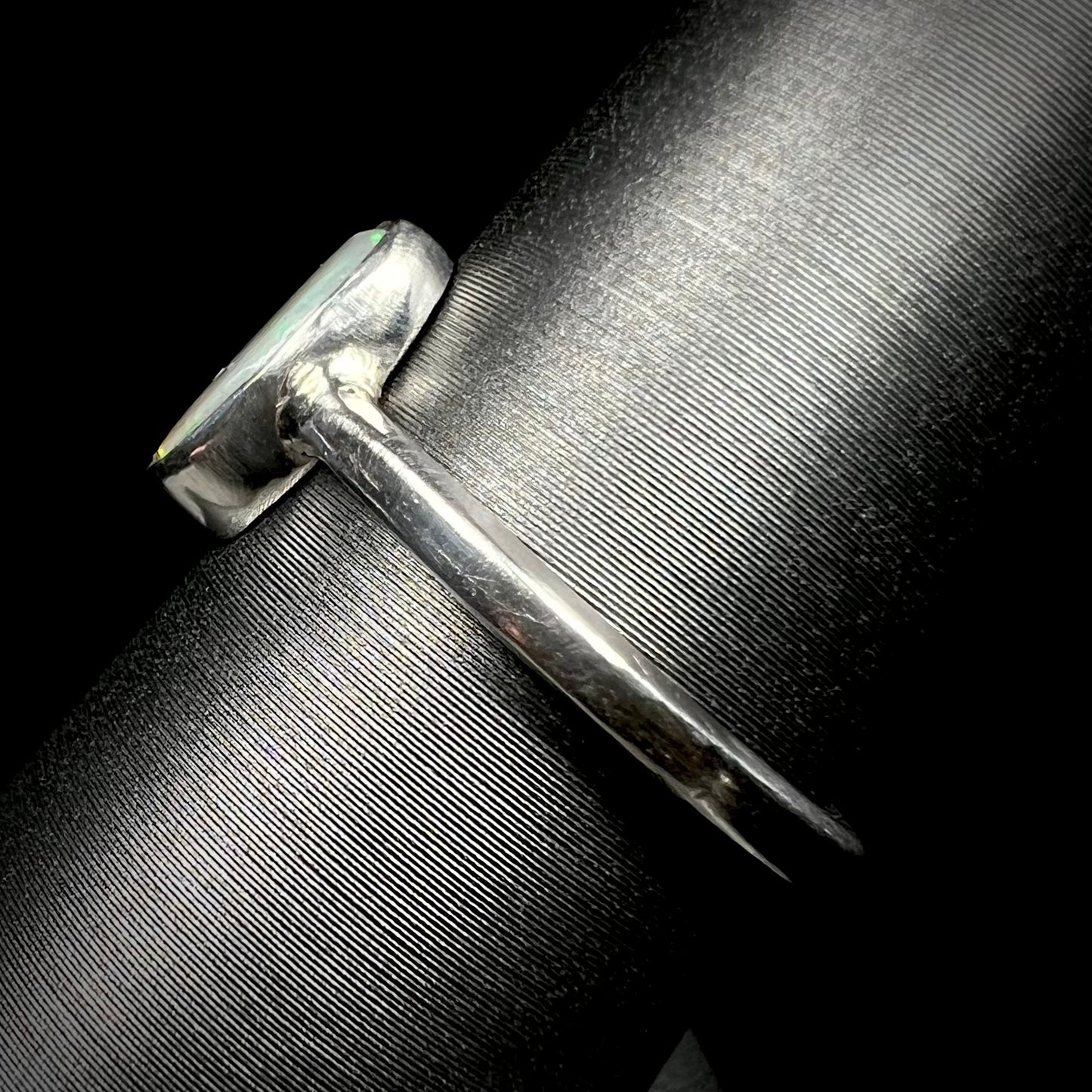 Side view of a handmade sterling silver opal solitaire ring on a ring display.  The ring's shank is in focus; the opal is not visible.