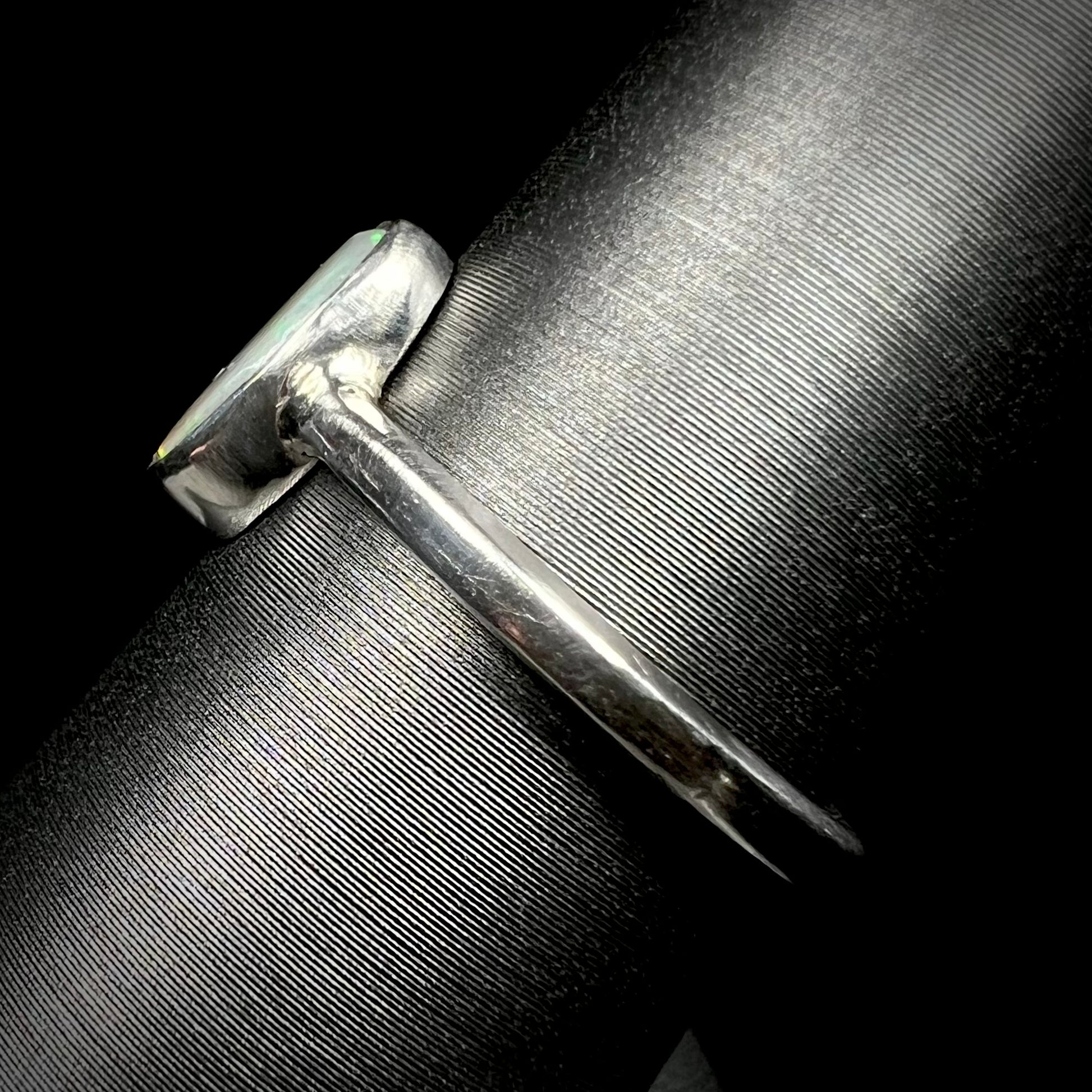 Side view of a handmade sterling silver opal solitaire ring on a ring display.  The ring's shank is in focus; the opal is not visible.