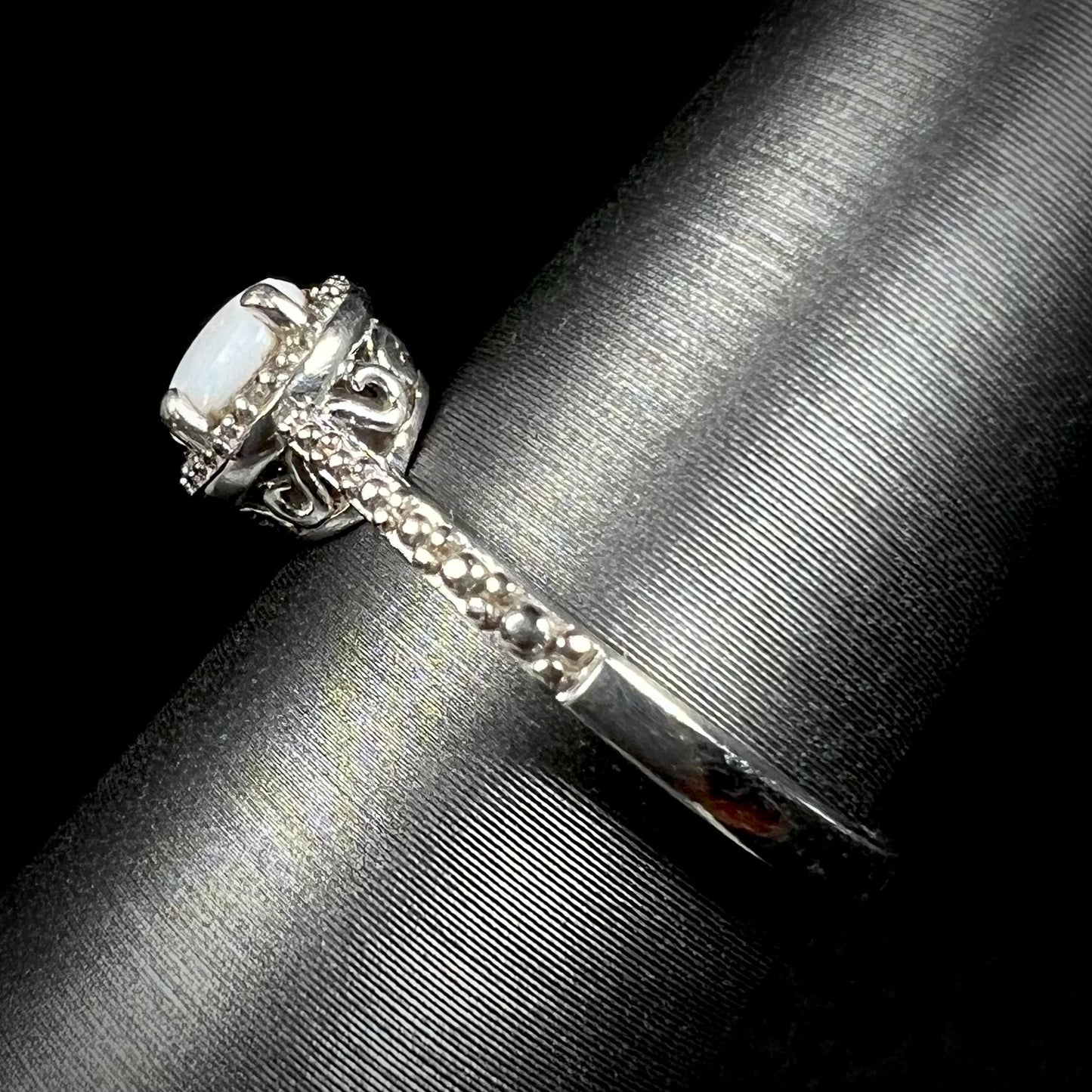 Side view of a sterling silver white opal and diamond ring with a halo design and filigree.