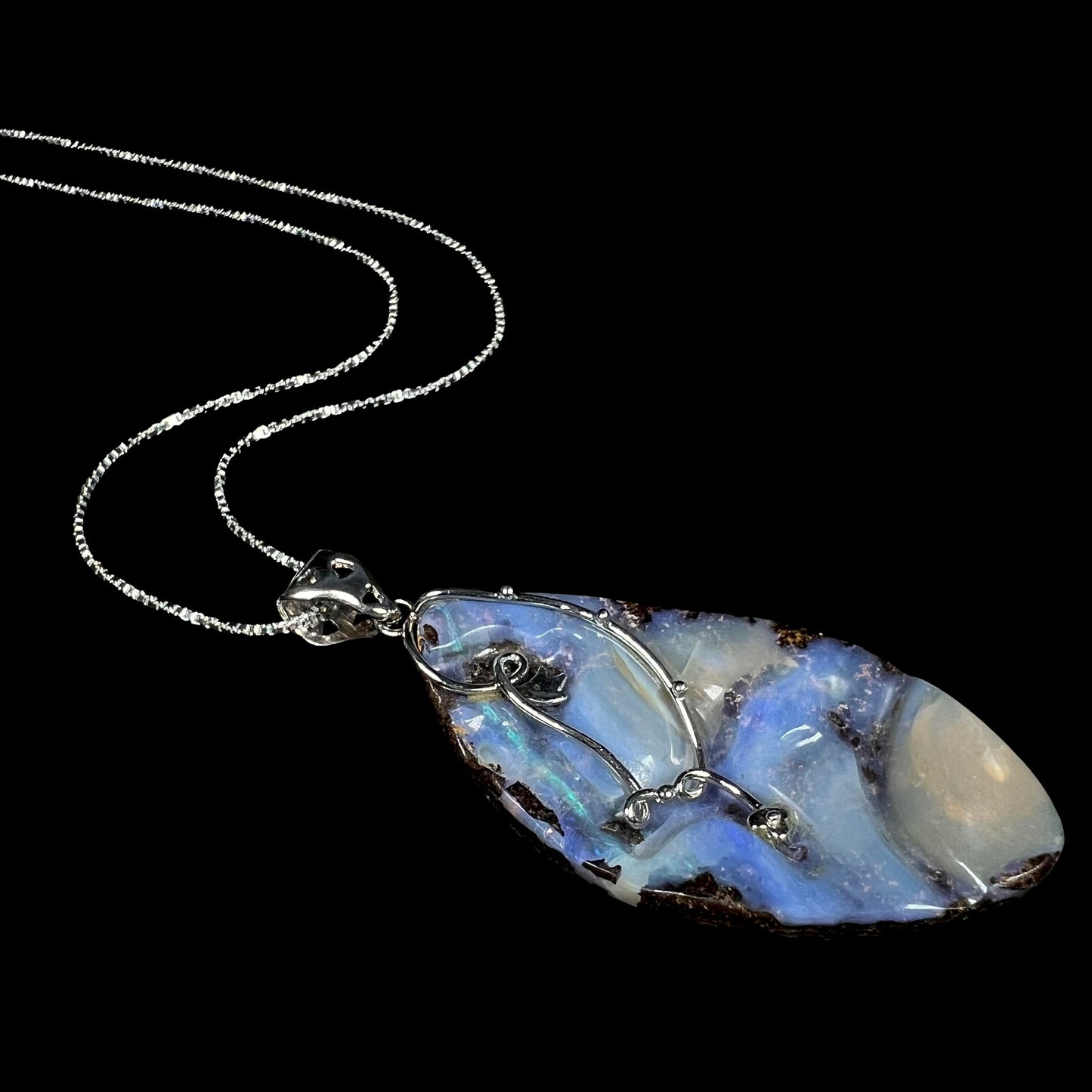 A sterling silver blue Australian boulder opal necklace, shown at an angle laying against a black background.