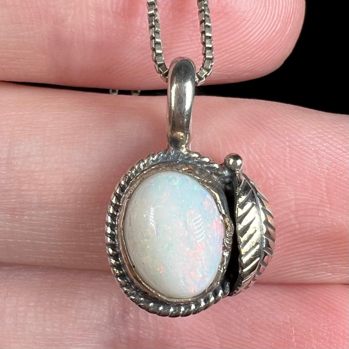 Close-up of white Australian opal pendant with handmade sterling silver Southwest leaf and rope-textured bezel design, held in hand