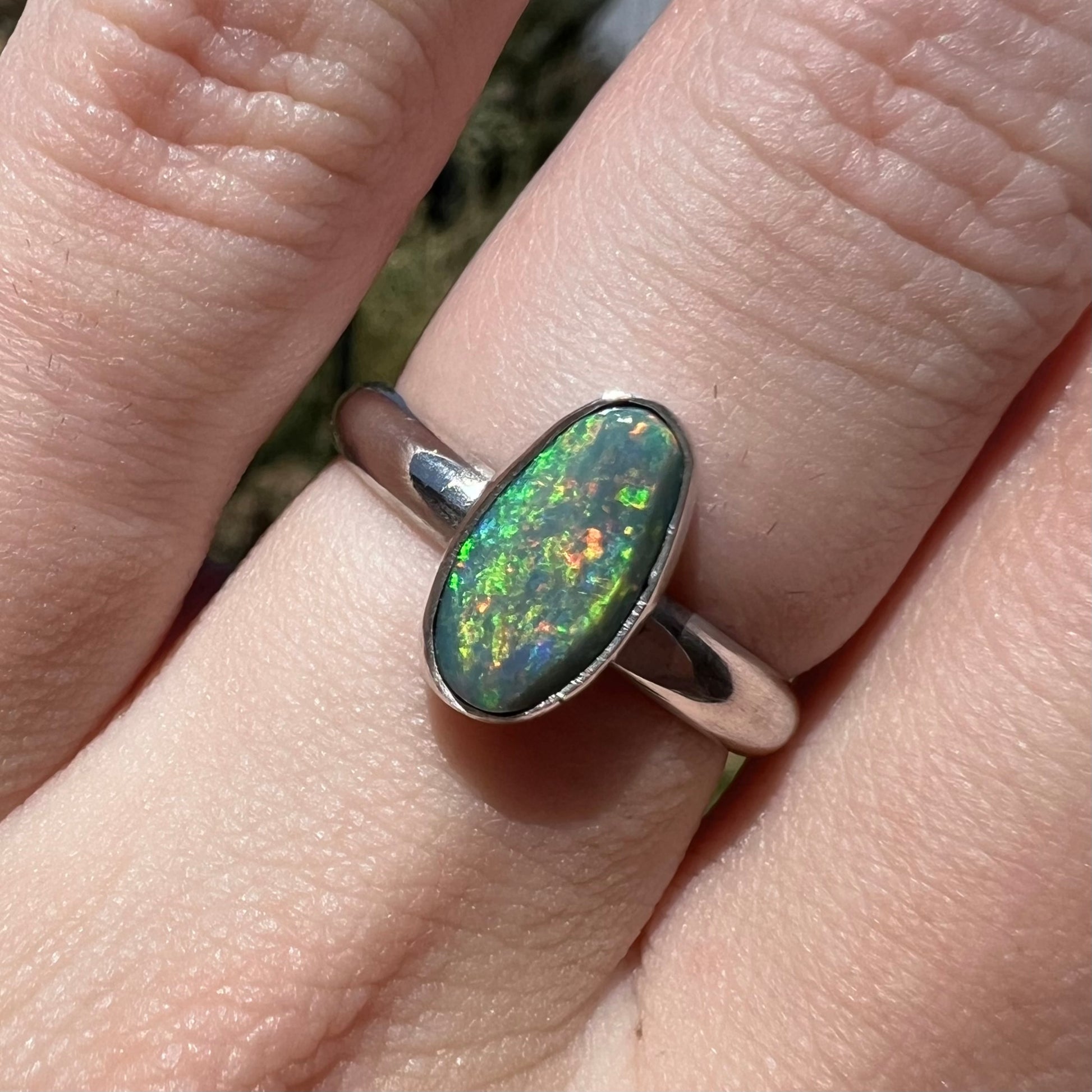 Close-up macro view of a women's sterling silver Australian opal solitaire ring in sunlight, worn on a finger.  The opal has green fire.