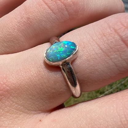 Angled close-up of a women's sterling silver Australian semi-crystal opal solitaire ring shown in sunlight on a finger.