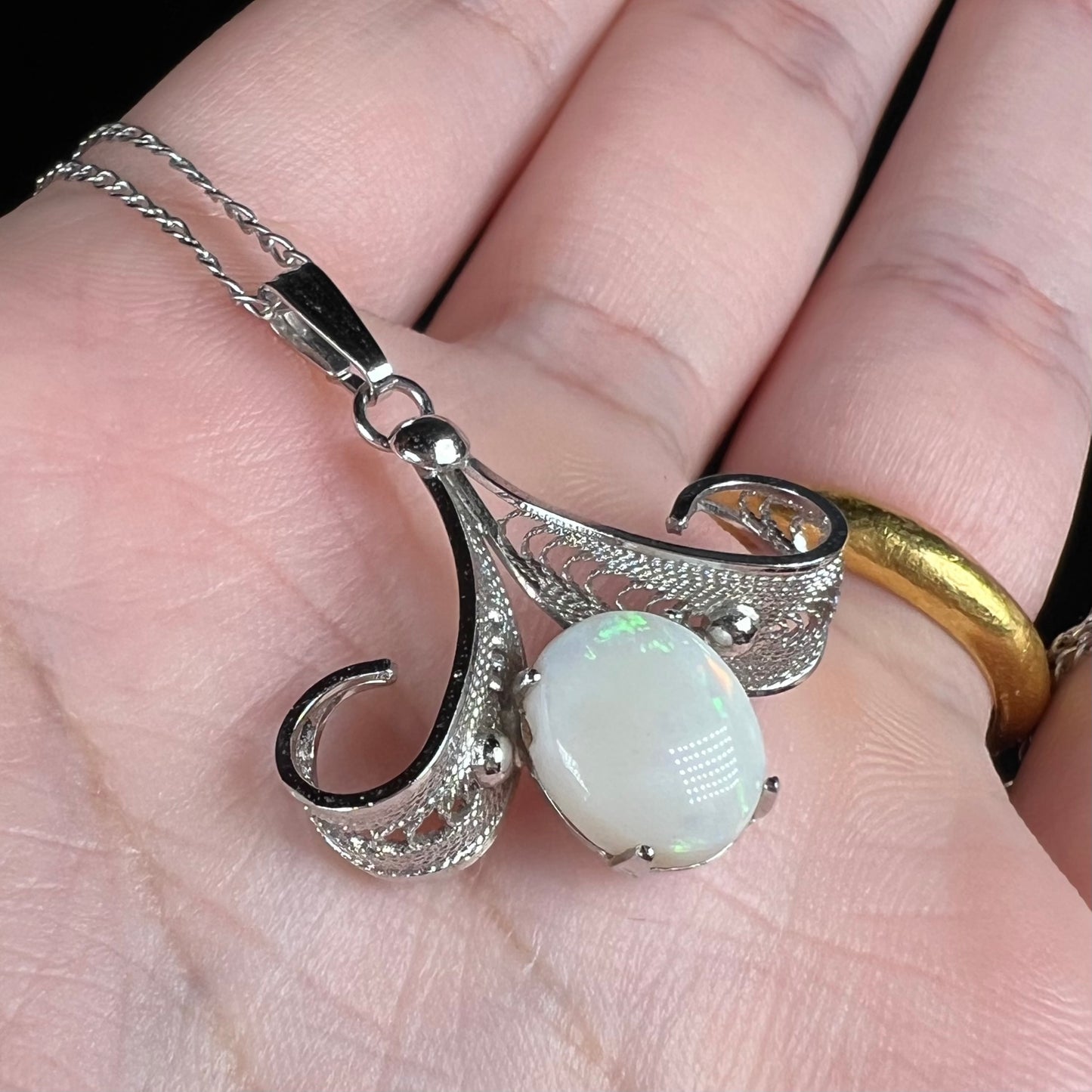 A Sorrento brand sterling silver Australian white opal pendant shown close-up from an angle in a hand.