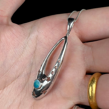 Angled close up of a sterling silver and opal doublet ballerina shoe necklace shown in a hand.