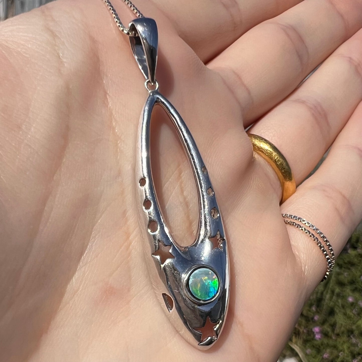 Close-up angled sunlit view of a sterling silver and opal doublet ballerina shoe necklace in a hand.
