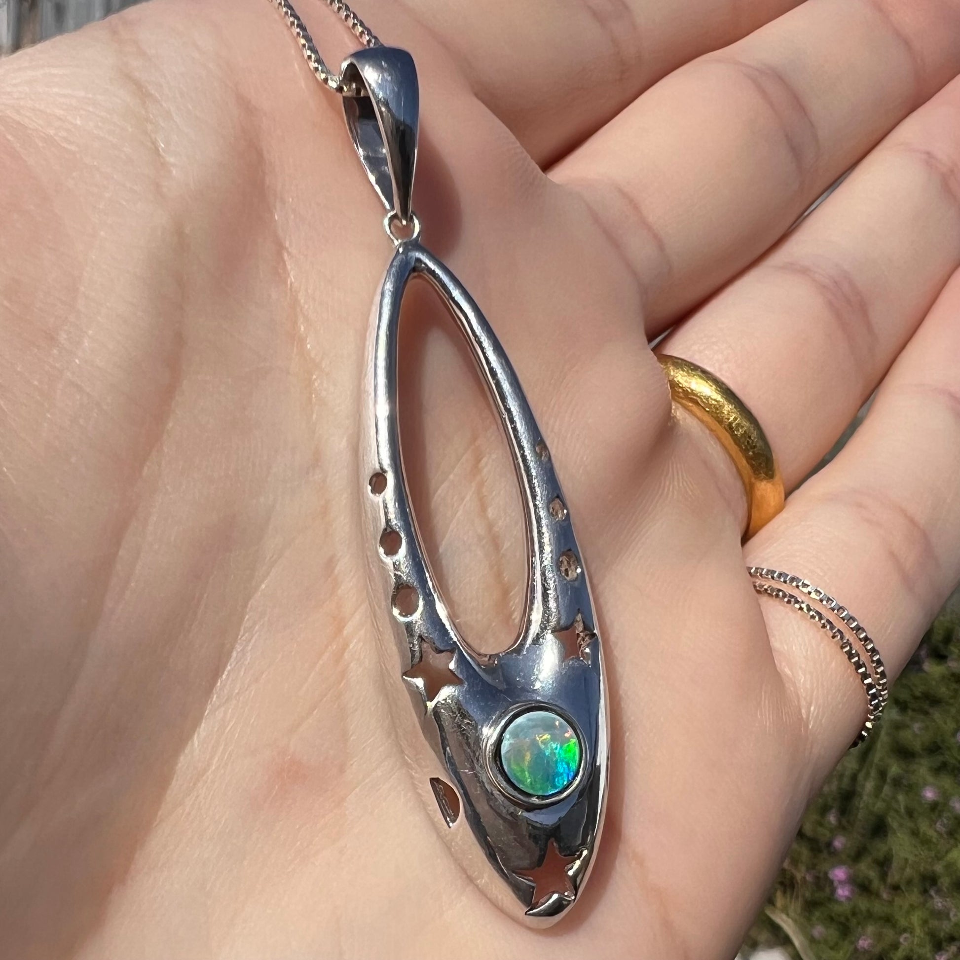 Close-up angled sunlit view of a sterling silver and opal doublet ballerina shoe necklace in a hand.