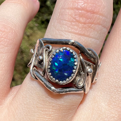 Close-up natural sunlit view of sterling silver black opal doublet ring with handmade leaf and vine design worn on finger