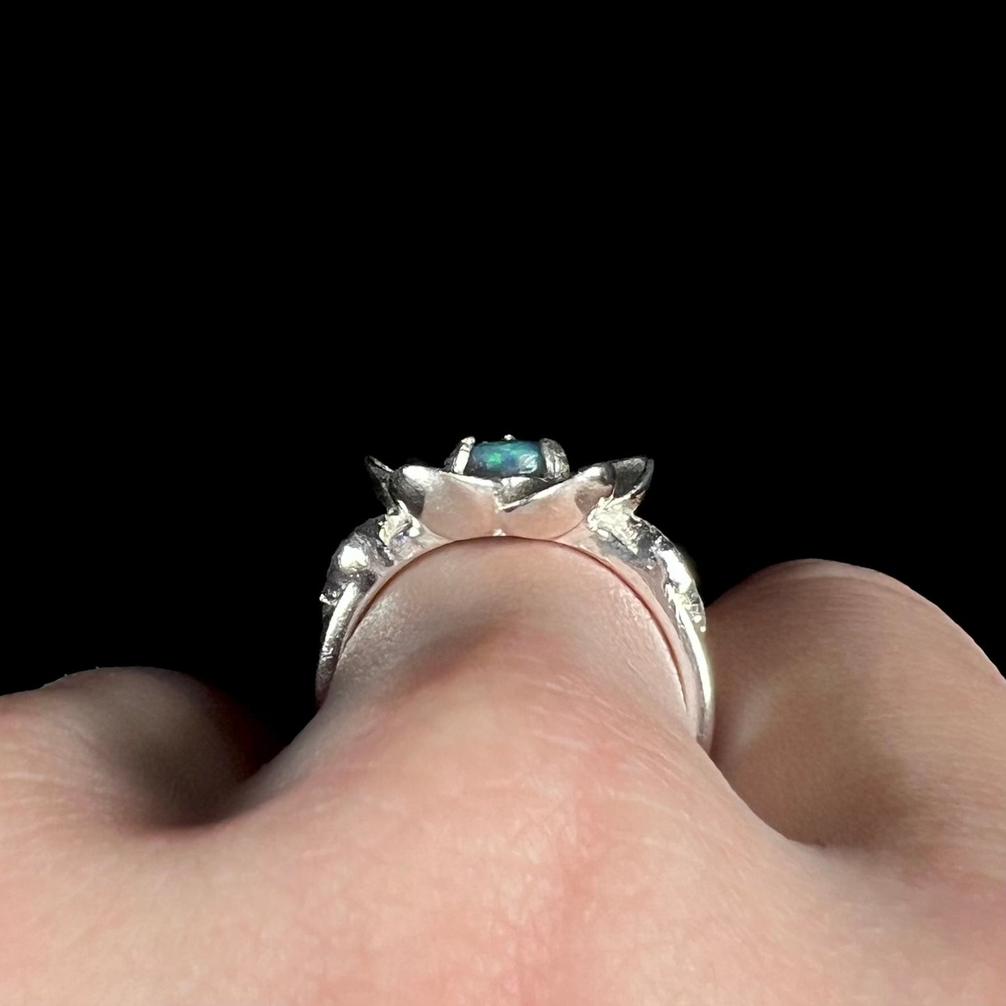 Side profile gallery view of silver black opal flower design ring, worn on hand