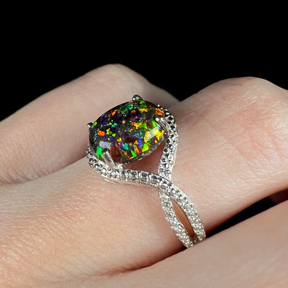 A lab-created black opal solitaire ring with green color play in sterling silver, shown at an angle on a hand.