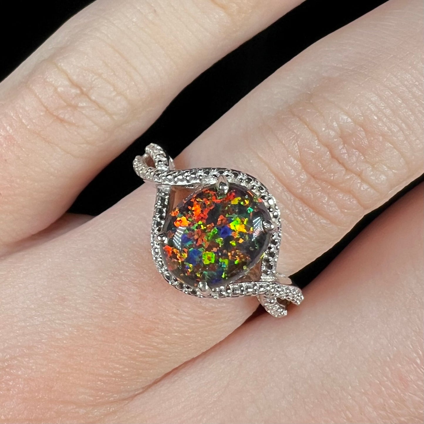 A lab-created black opal solitaire ring with red color play in sterling silver, shown close-up on a hand.