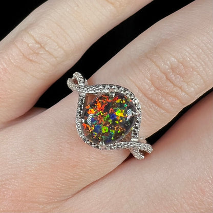 A lab-created black opal solitaire ring with red color play in sterling silver, shown close-up on a hand.