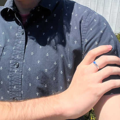 Close-up of person resting hand on opposing shoulder wearing sterling silver blue opal solitaire ring in sunlight