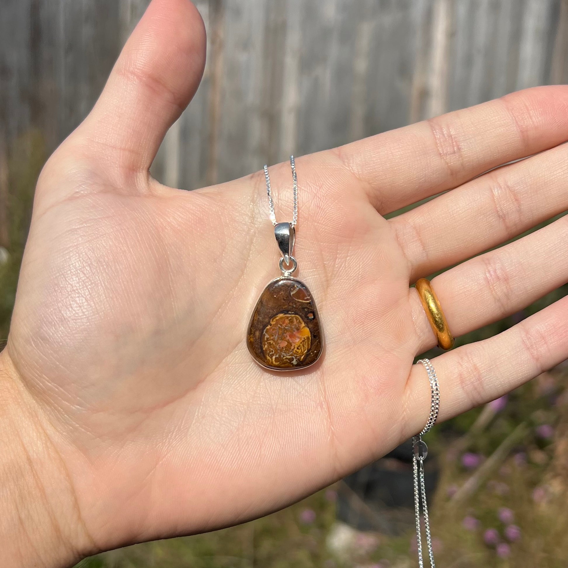 A Yowah nut boulder opal necklace in sterling silver, held in a hand and shown in the sunlight.