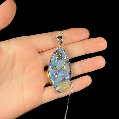 A large, blue Australian boulder opal necklace in sterling silver, shown in a hand against a black background.