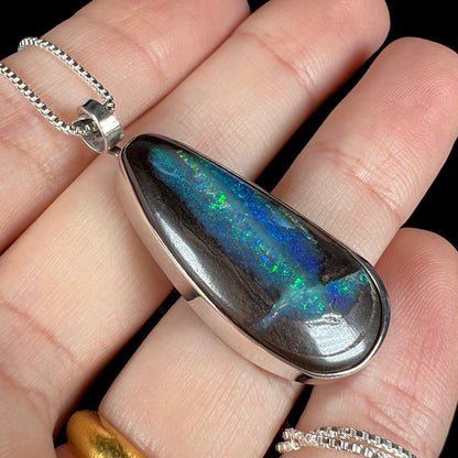 Close-up of an Australian boulder opal pendant with glittering blue and green color play, shown at an angle in a hand.