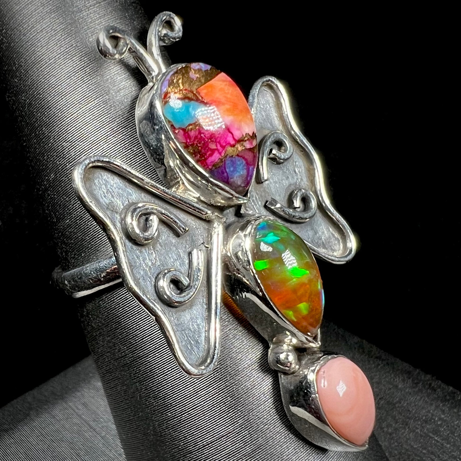 A sterling silver butterfly ring set with different varieties of opals, shown at an angle.