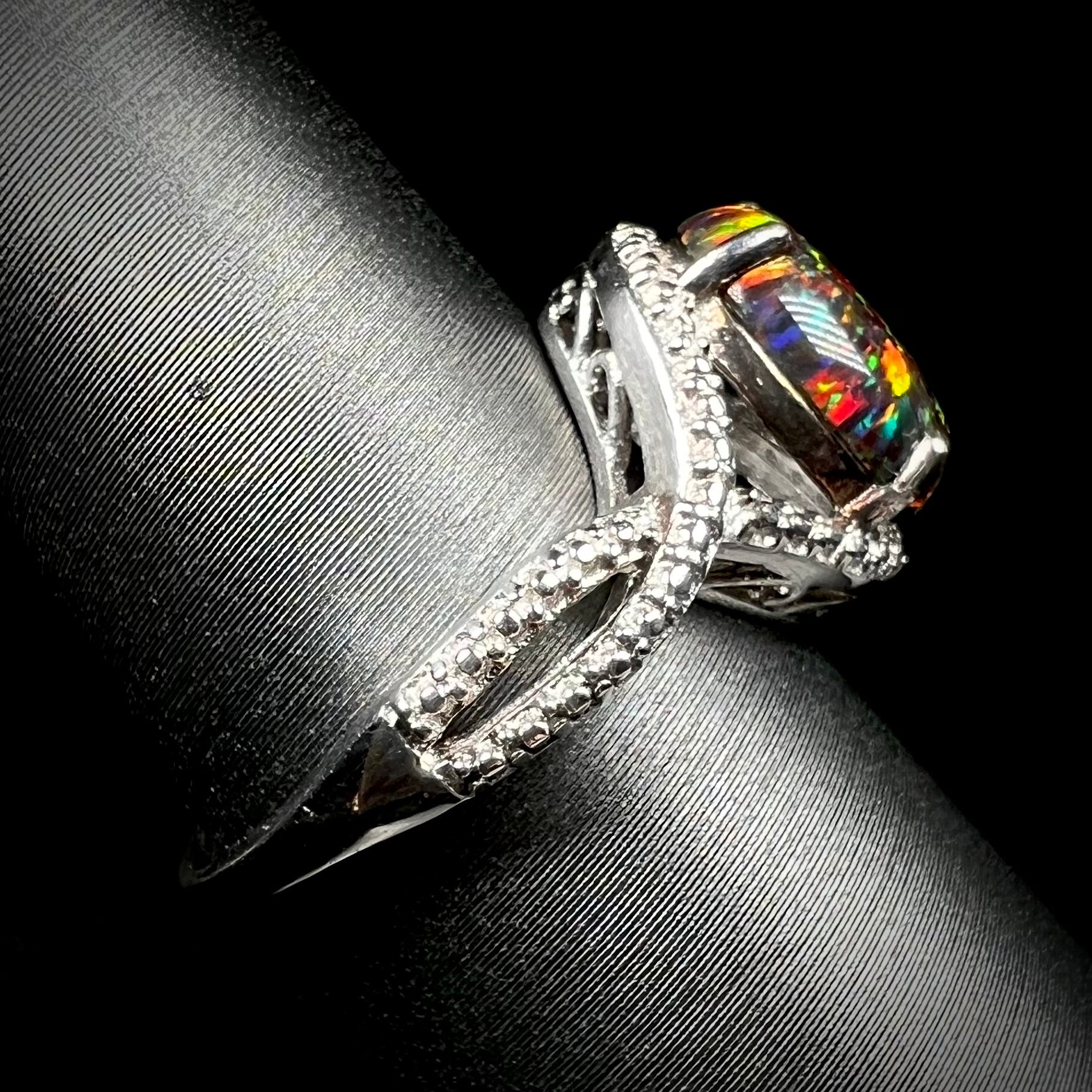 A lab-created black opal solitaire ring with red color play in sterling silver shown from the side on a ring display.