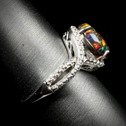 A lab-created black opal solitaire ring with red color play in sterling silver shown from the side on a ring display.