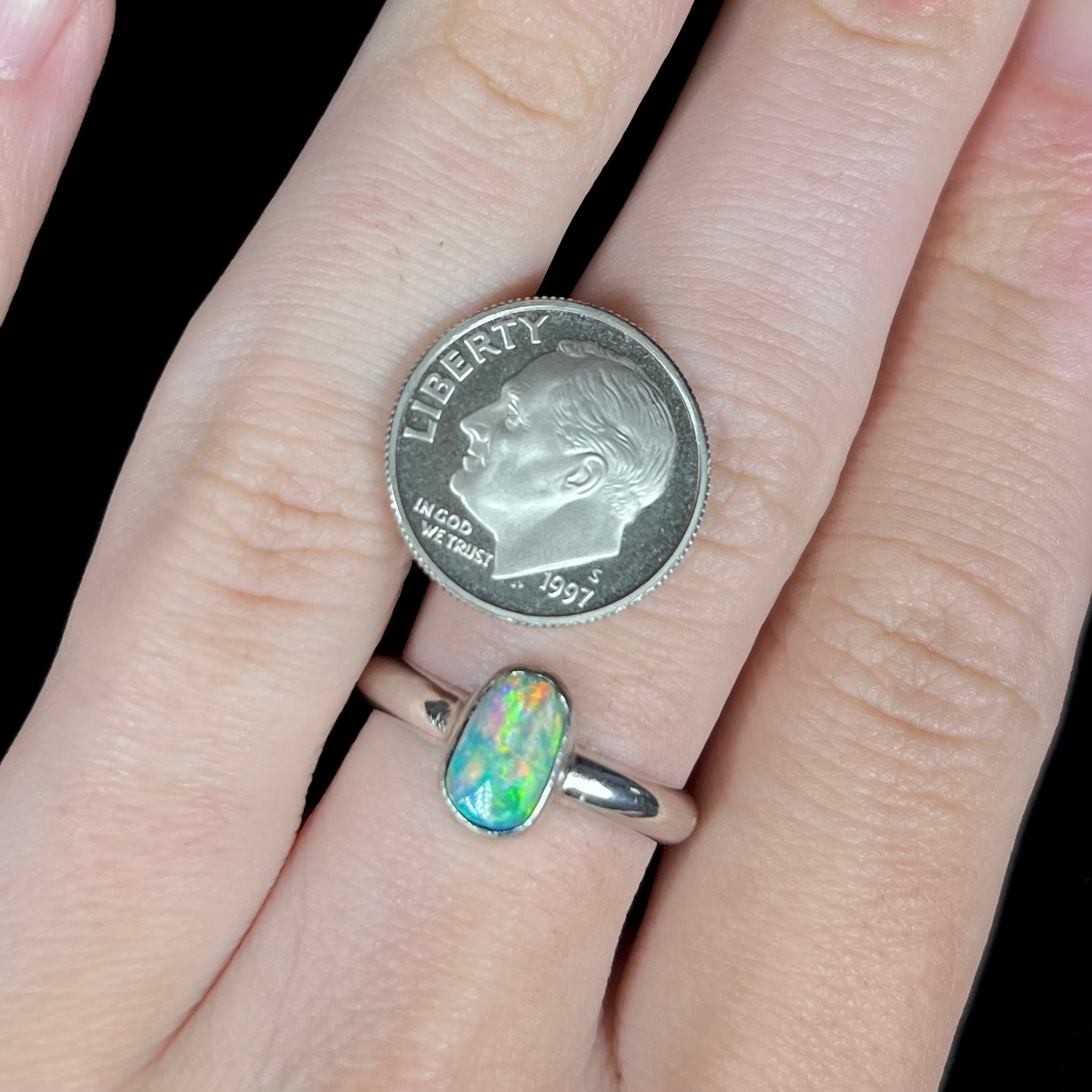 Freeform shaped silver Australian crystal opal ring worn on hand next to US dime coin for scale