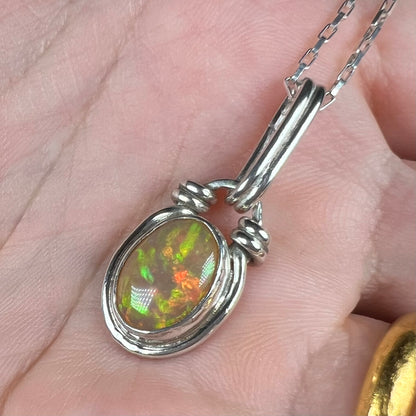 A sterling silver Ethiopian fire opal pendant shown close-up in a hand from an angle.