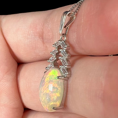Side view close-up of silver Ethiopian opal and emerald cut CZ drop pendant, held in hand