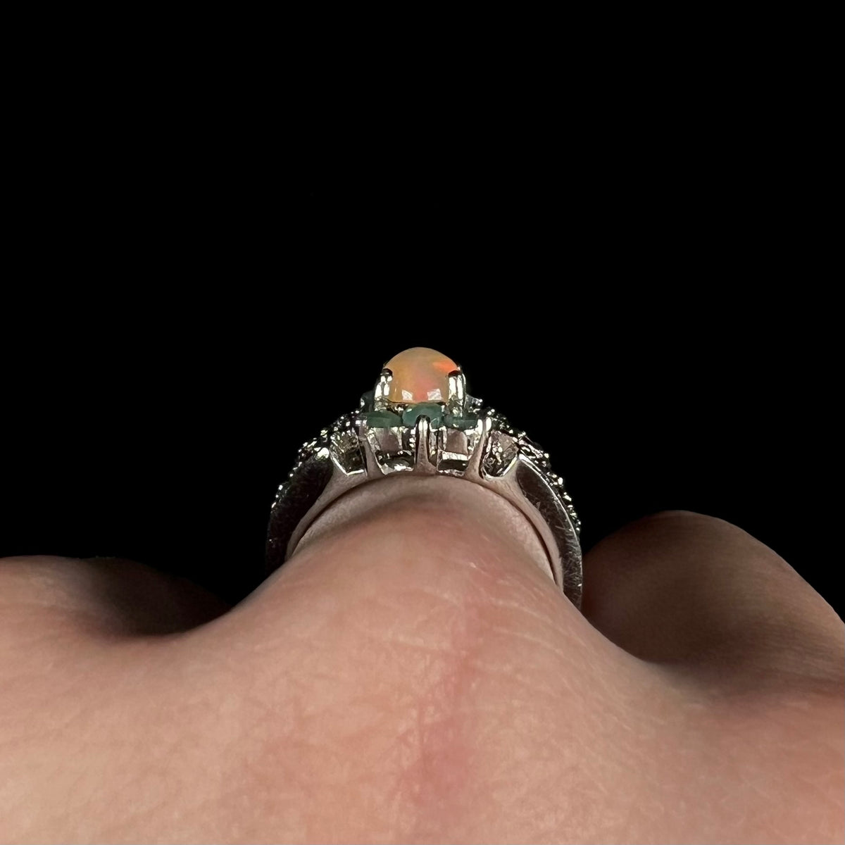 Side gallery profile view of sterling silver Ethiopian opal and emerald ring, worn on finger