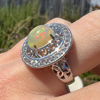 Close-up of a silver Ethiopian opal filigree ring worn on a finger in the sunlight.