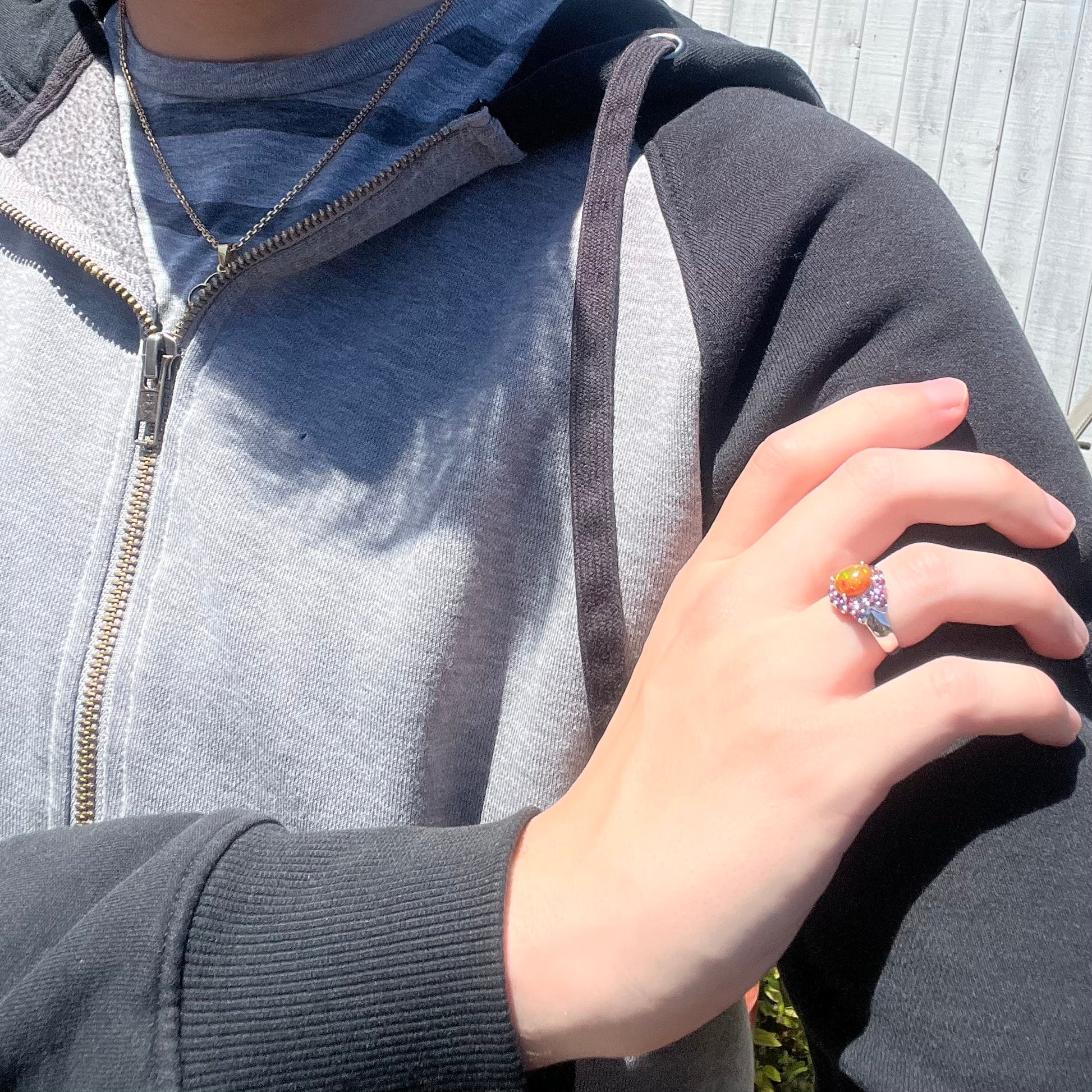 Close-up of person resting hand on opposing shoulder in sunlight wearing silver Ethiopian opal and purple rhodolite garnet ring