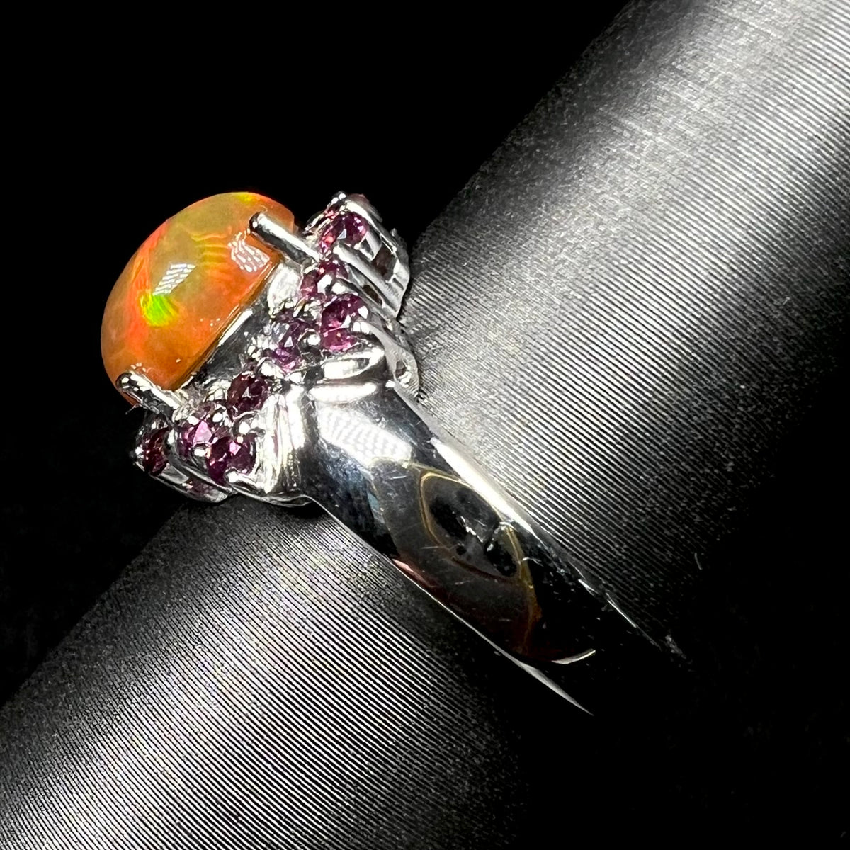 Side view of silver Ethiopian opal and garnet ring on display, focusing on ring's polished shank