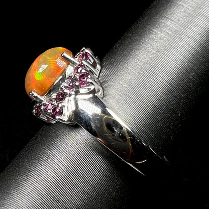 Side view of silver Ethiopian opal and garnet ring on display, focusing on ring's polished shank