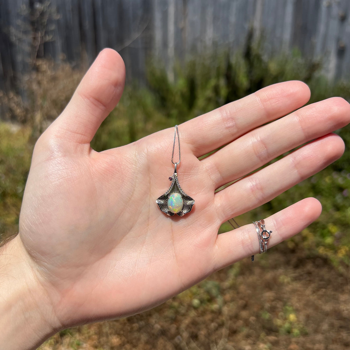 Hand holding sterling silver Ethiopian opal necklace with Chinese ginko leaf motif under natural sunlight